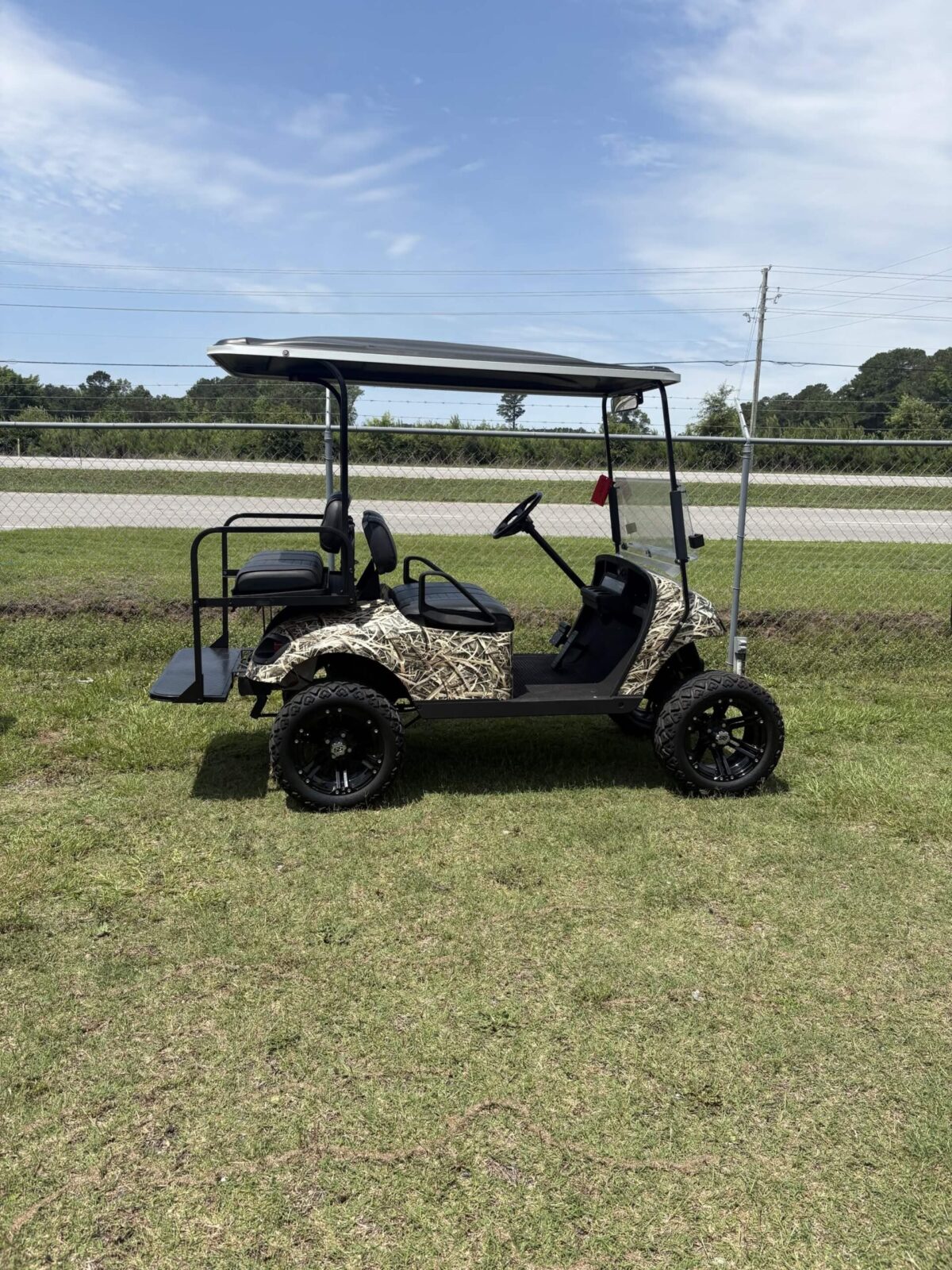 2013 E-Z-GO 48V golf cart with camouflage body wrap, lifted suspension, black alloy wheels, and rear flip seat parked on grass outdoors.