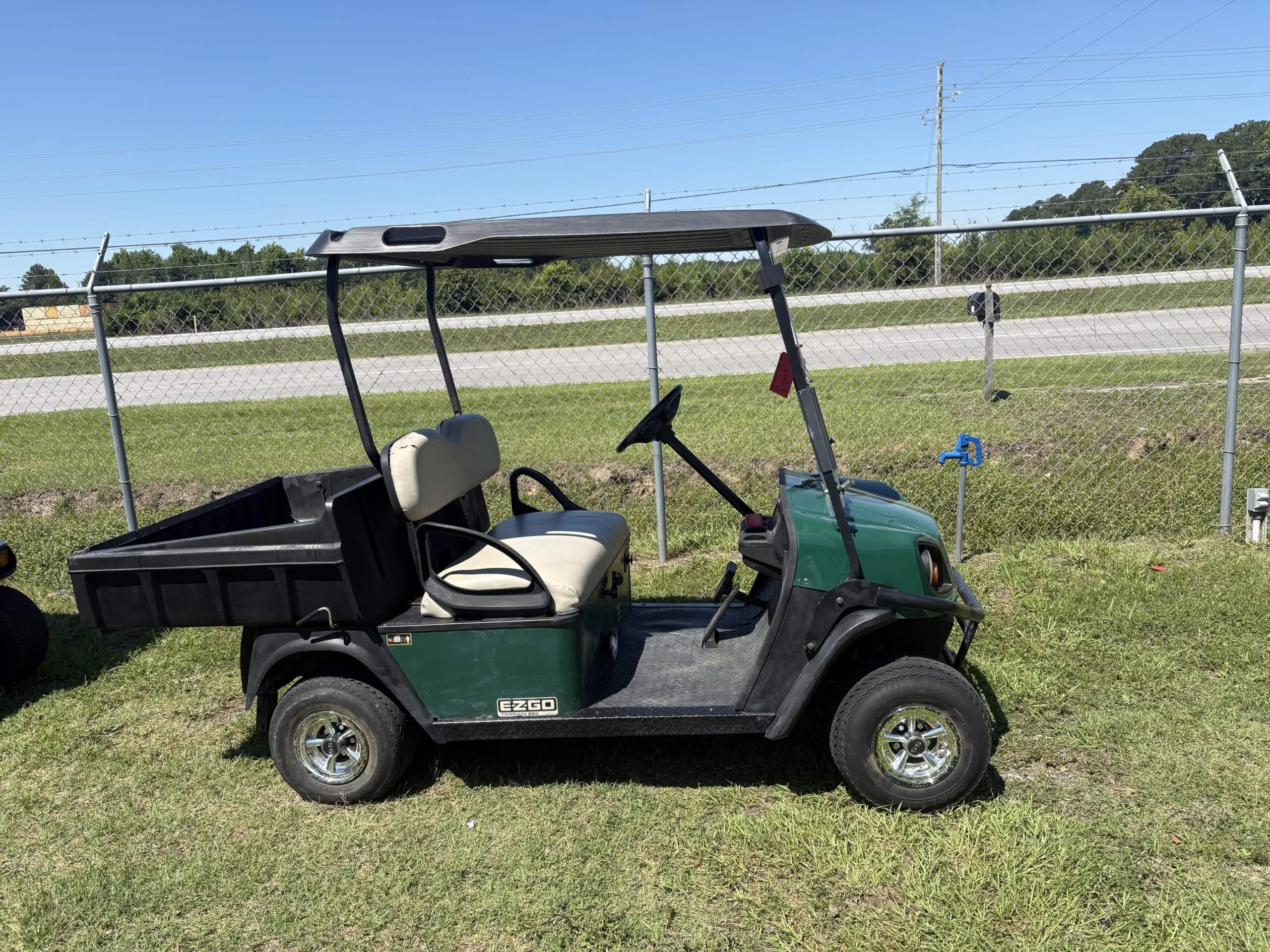 2016 E-Z-GO Terrain 250 gas golf cart with a rear utility dump bed, green body, beige seats, and all-terrain tires parked on grass.