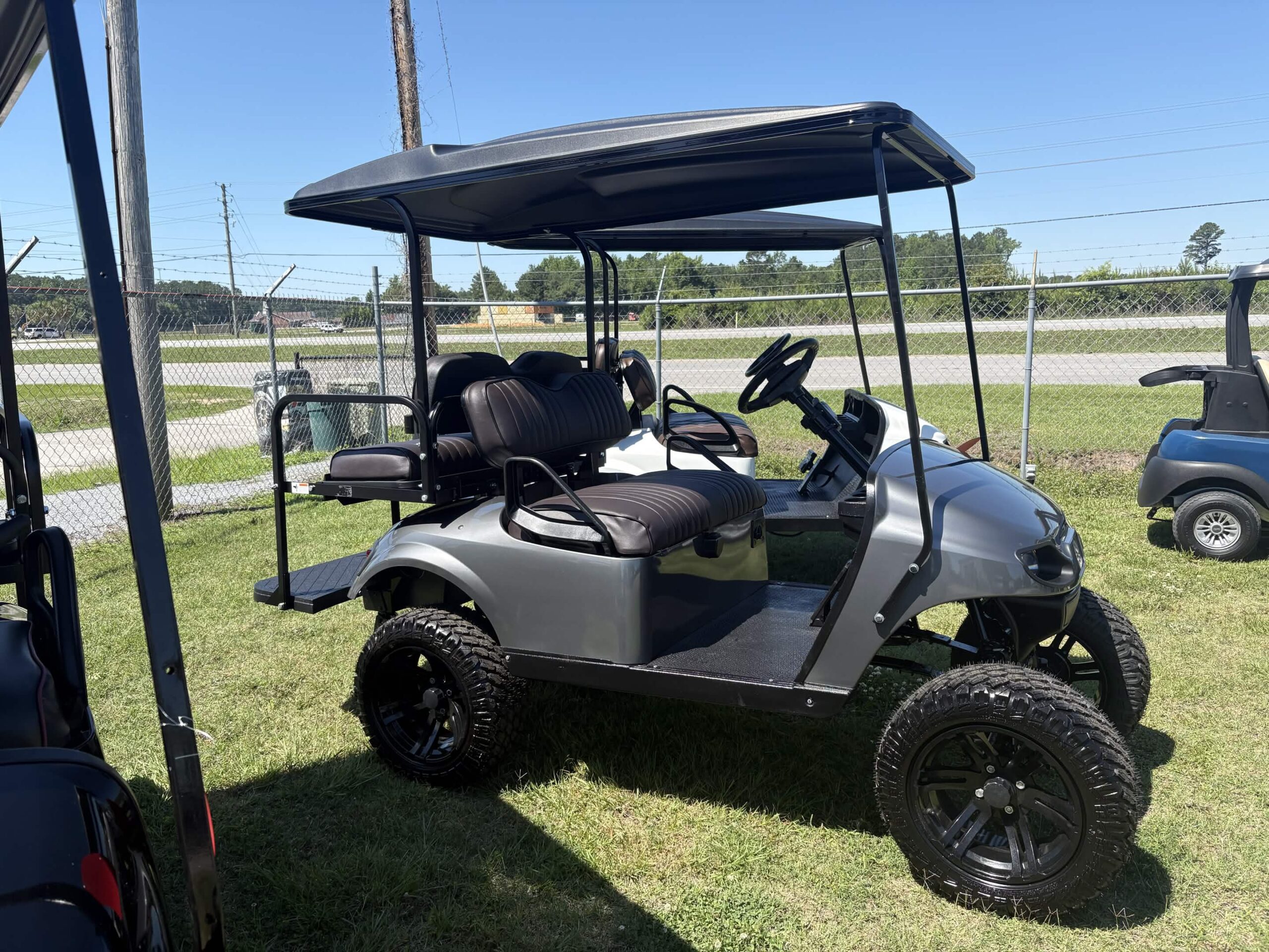 2017 E-Z-GO Freedom golf cart with a lifted suspension, premium black wheels, gray body, black seats, and rear flip seat parked outdoors.