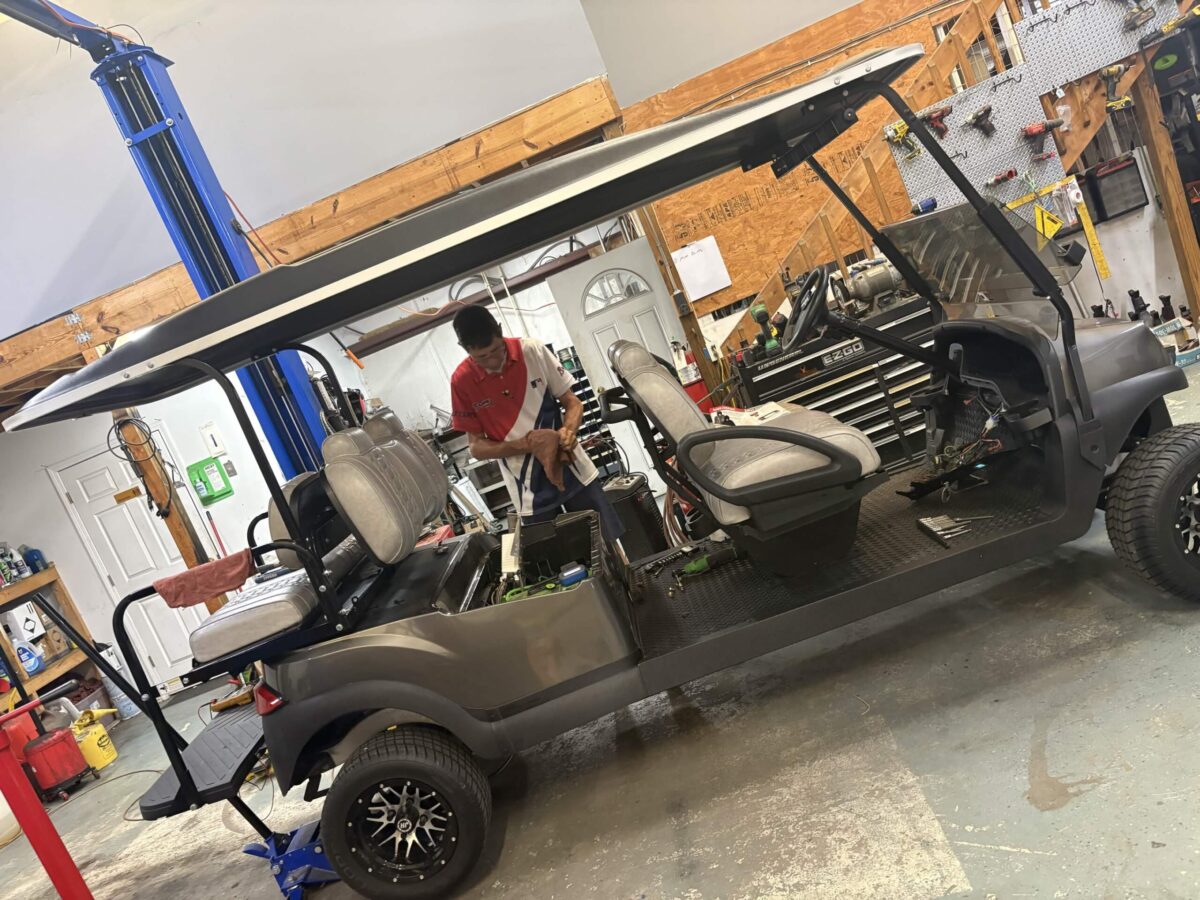 Technician working on a golf cart during service and maintenance inside a professional repair shop.
