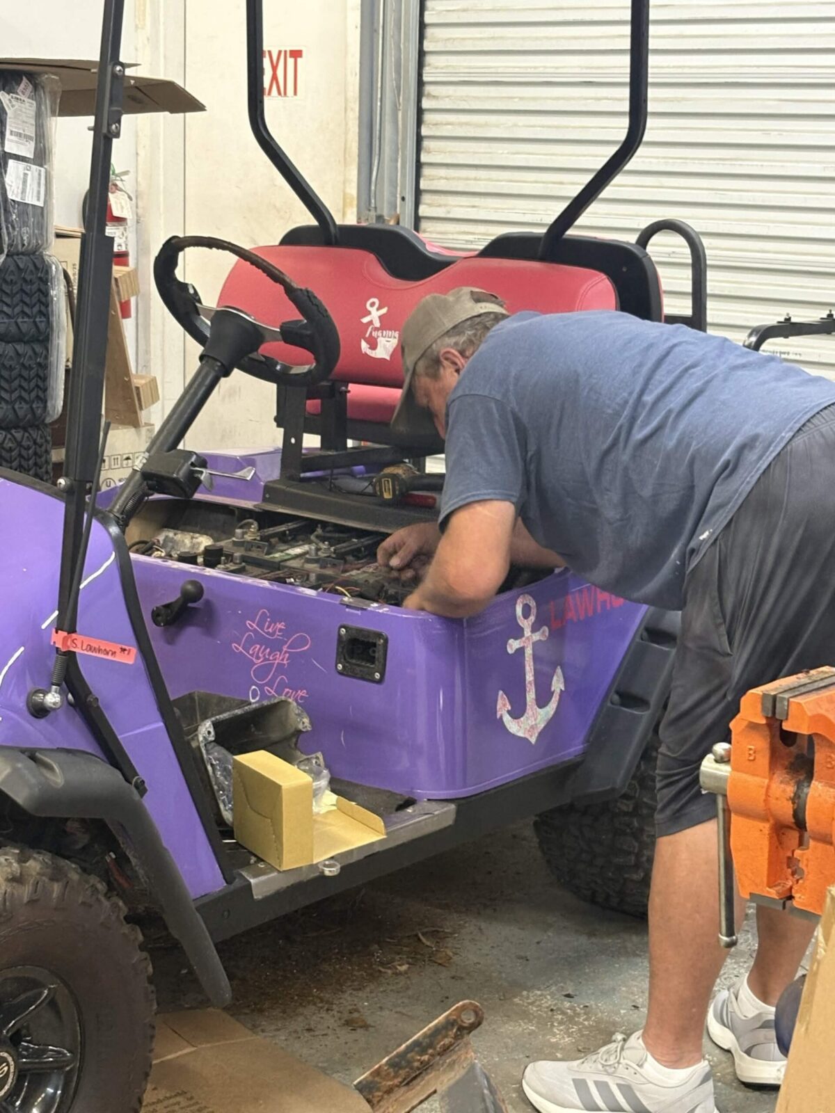 Technician performing maintenance on a custom purple golf cart with rear seat and lifted tires inside a service shop.